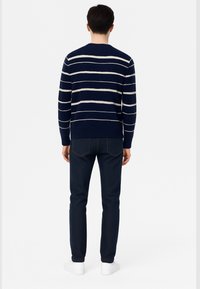 Maglione a righe navy con strisce orizzontali crema, collo rotondo, polsini a coste, abbinato a jeans blu scuro e sneakers bianche. Vista posteriore.