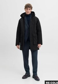 Čierna nepremokavá parka s kapucňou, s dvoma prednými vreckami, elegantným dizajnom, a v kombinácii s námorníckym svetrom a strihovými nohavicami.