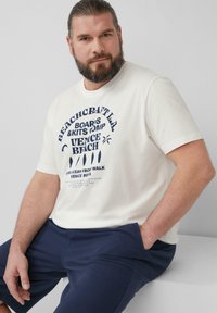 Lichtcreme t-shirt met marineblauwe grafische tekst "VENICE BEACH," gecombineerd met donkerblauwe shorts. Eenvoudige ronde hals, korte mouwen.