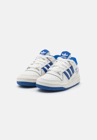 White sneakers with blue accents, featuring three blue stripes, perforated toe design, and a textured rubber sole. White laces and logo on tongue.