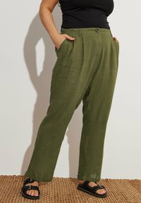 Olivgrön, löst sittande byxor med sidofickor; veckad framdel; lättviktsmaterial med en texturerad yta; matchas med svarta sandaler.