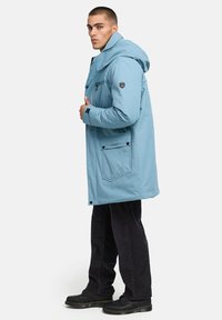 Gaiši zils ūdensizturīgs parka mētelis ar kapuci, lielām priekšējām kabatām un spiedpogu aizdari. Melni akcenti un unikāls logo uz piedurknes.