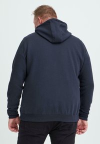 Marineblå hettegenser med en avslappet passform, ribbestrikkede mansjetter og glatt tekstur. Bakfra sett uten synlige logoer eller mønstre.