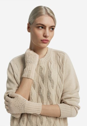 Beige fingerløse handsker lavet af strikket stof, med glitrende detaljer og ribstrikkede manchetter, båret sammen med en matchende kabelstrikket sweater.