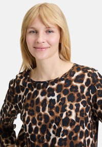 Leopardenmuster-Oberteil mit einer strukturierten Stoffoberfläche, rundem Ausschnitt und Dreiviertelärmeln in Braun-, Schwarz- und Weißtönen.
