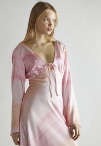 Vestido de manga larga en suave tela rosa con escote en V y detalle de cordón en el busto. Presenta una textura lisa y un patrón degradado.