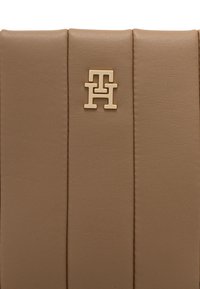 Bolso de cuero beige con tres pliegues verticales y un logo dorado en el frente. Textura suave con un brillo sutil.