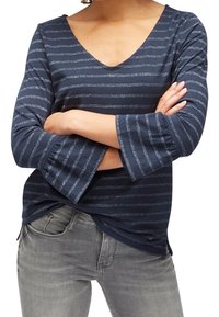 Top a maniche lunghe blu navy con scollatura a V e strisce orizzontali argentate; polsini svasati e tessuto morbido e leggero. Abbinato a jeans grigi.