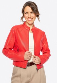 Veste en cuir rouge avec un col montant, fermeture éclair à l'avant et deux poches latérales. Finition avec des coutures visibles et une coupe courte.