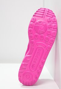Pink rubber shoe sole featuring textured grip patterns, circular accents, and embossed "adidas" logo, angled against a white background.