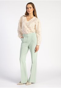 Lichtbeige textuur blouse met een v-hals en lange mouwen, gecombineerd met hooggepaste mintgroene broek met scherpe plooien.