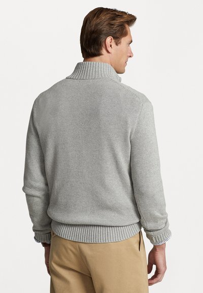 Grauer Strickpullover mit hohem Kragen und gerippten Ärmelabschlüssen. Der Stoff hat eine strukturierte Oberfläche und der Saum zeigt ein geripptes Design.