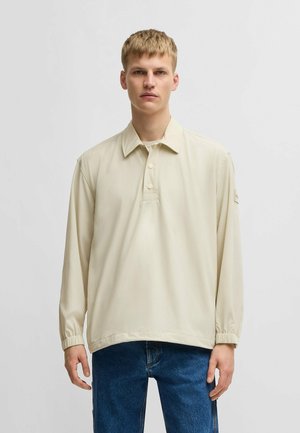 Light beige long-sleeve polo shirt with a collared neck and three buttons, featuring elastic cuffs and a relaxed fit.