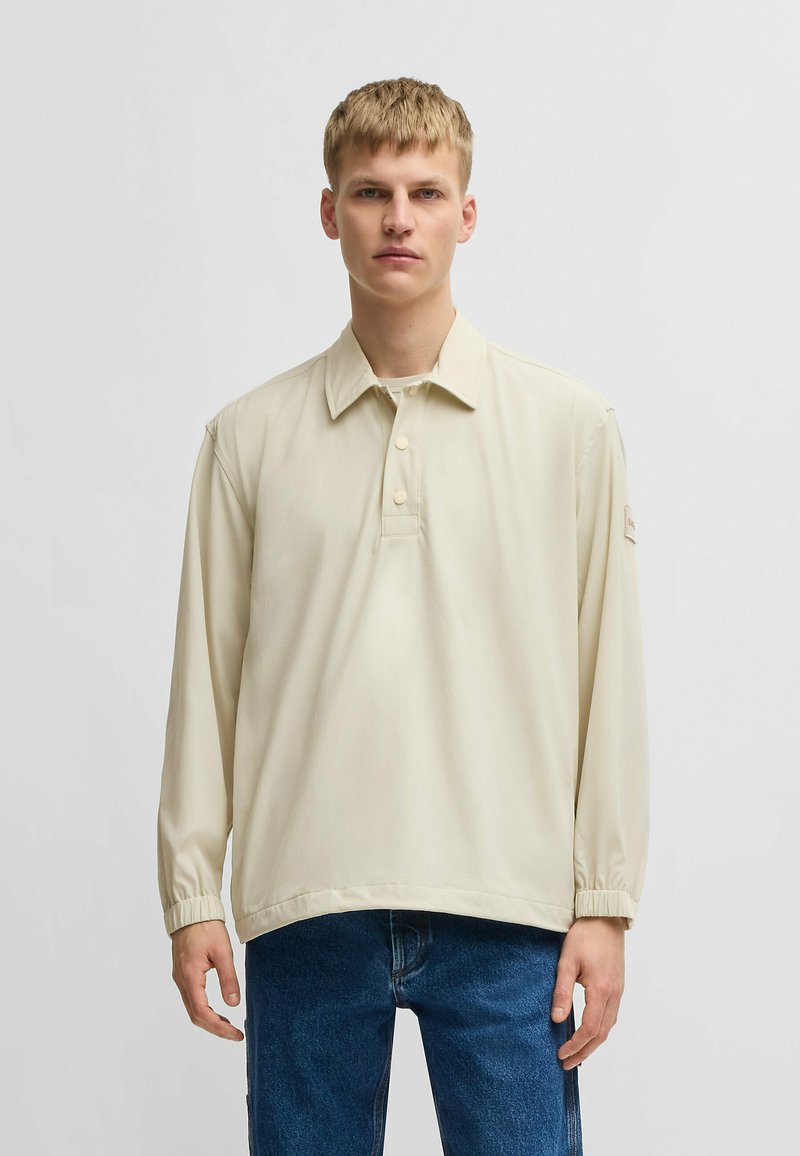 Hellbeige Langarm-Polohemd mit Kragen und drei Knöpfen, ausgestattet mit elastischen Bündchen und einem lockeren Schnitt.