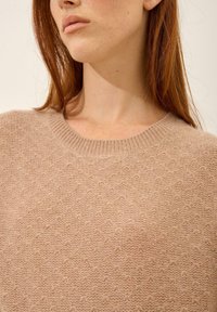 Beige gebreide trui met een ronde hals, een textuur oppervlak en een relaxte pasvorm. Het materiaal lijkt zacht en warm met subtiele details.