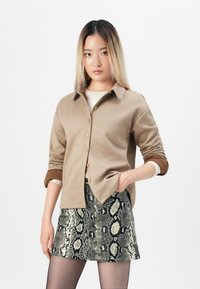 Light brown button-up shirt with a collar and rolled sleeves, paired with a patterned snake print skirt featuring black and cream tones.