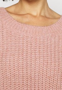 Różowy, dziergany sweter z szerokim, prążkowanym dekoltem i miękką fakturą. Charakteryzuje się luźnym, swobodnym krojem oraz pionowym wzorem ściegów.