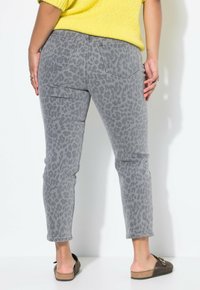 Jeans de leopardo gris con corte ajustado, que cuentan con bolsillos traseros y son de largo hasta el tobillo. Combinados con un suéter de punto amarillo y zapatos planos.