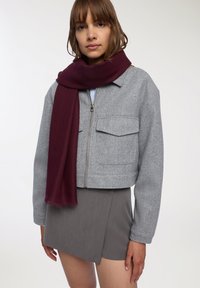 Przycięta szara polarowa kurtka z dwoma przednimi kieszeniami, zestawiona z długim bordowym szalikiem w prążki i szaro-mini spódnicą.