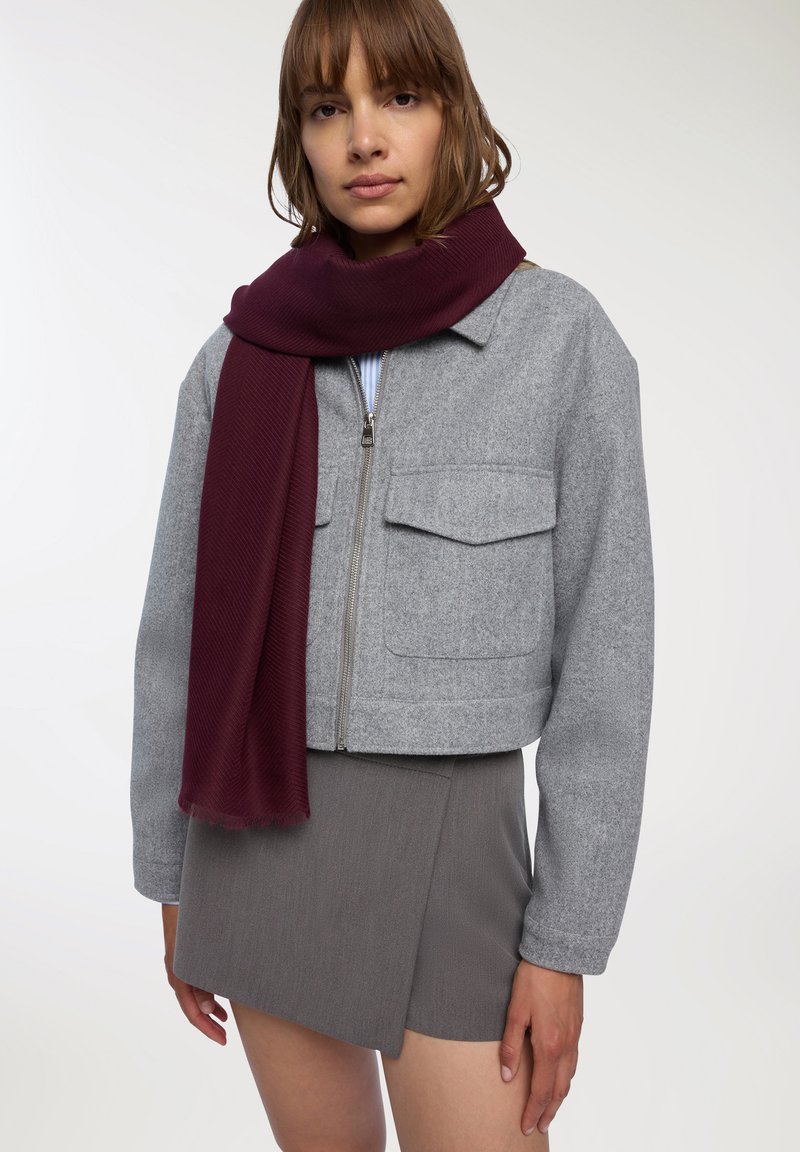 Przycięta szara polarowa kurtka z dwoma przednimi kieszeniami, zestawiona z długim bordowym szalikiem w prążki i szaro-mini spódnicą.