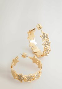 Cercei din aur în formă de cercei cu inele, prezentând forme de stea interconectate. Unul dintre cercei are pietre strălucitoare transparente pentru un plus de strălucire. Textură de metal neted.