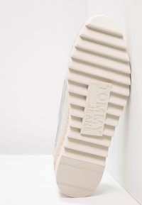 Semelle argentée avec un motif en caoutchouc blanc texturé, avec "TOMMY JEANS" embossé sur le côté. Design lisse et moderne.