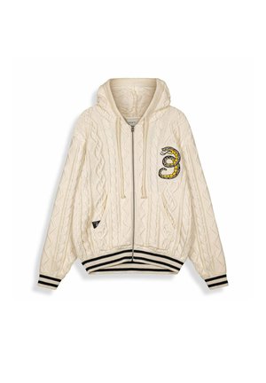 Kremowa bluza z kapturem na zamek z grubym splotem, z czarno-białymi paskowanymi mankietami i dołem, ozdobiona naszywką z owiniętym w kółko wężem na lewym kieszeni piersiowej.