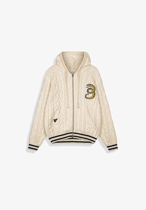 Kremowa bluza z kapturem na zamek z grubym splotem, z czarno-białymi paskowanymi mankietami i dołem, ozdobiona naszywką z owiniętym w kółko wężem na lewym kieszeni piersiowej.