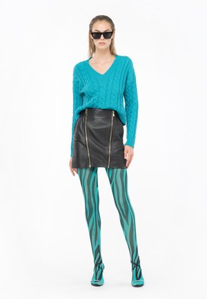 Maglione azzurro a treccia, mini gonna in pelle nera con cerniere, leggings a righe turchesi e neri, occhiali da sole neri, scarpe turchesi.