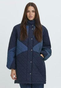 Chaqueta acolchada de color azul marino con un patrón geométrico en tonos variados de azul, cuello alto, botones a presión y bolsillos laterales.