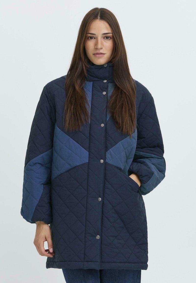 Chaqueta acolchada de color azul marino con un patrón geométrico en tonos variados de azul, cuello alto, botones a presión y bolsillos laterales.
