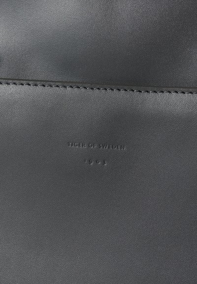 Υφή μαύρου δέρματος με ματ φινίρισμα, με ανάγλυφο λογότυπο "Tiger of Sweden" και την έτος "1903" από κάτω. Απλή ραφή λεπτομέρεια.