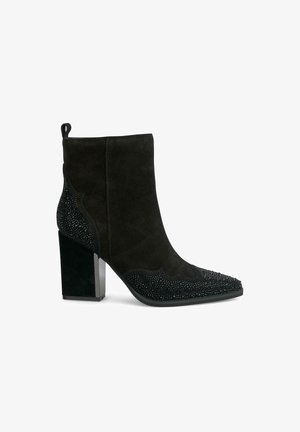 Schwarze Ankle Boots mit Blockabsatz, aus Wildleder, mit einem Perlenmuster an der Spitze und an den Seiten. Spitz zulaufende Zehenpartie und Zuglasche an der Ferse.