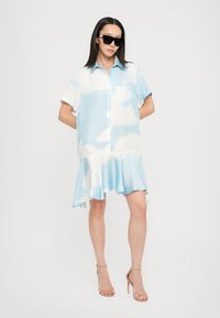 Rochie cu mânecă scurtă de culoare bleu deschis, cu un model de nori, având un guler cu nasturi, un buzunar pe piept și un tiv evazat. Purtați ochelari de soare negri.