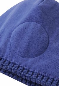 Close-up of a blue fleece fabric with a circular padded area above a ribbed knit edge, showing texture and stitching details.