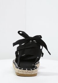 Sandal espadrille nera con tomaia in tessuto e suola in juta intrecciata. Presenta lacci alla caviglia, design con tallone aperto e una soletta testurizzata.