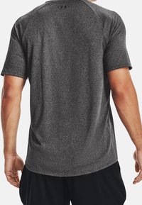 Camiseta deportiva gris de manga corta con textura lisa, que presenta un cuello redondo y mangas raglán. Logotipo en la parte posterior del cuello.
