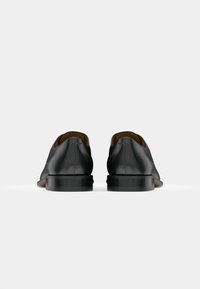 Zapatos de cuero negros con un diseño elegante, punta redonda y un tacón bajo de goma. La parte trasera tiene un acabado suave y detalles de costura mínimos.