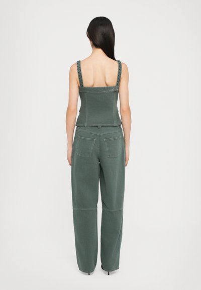 Grünes Denim-Outfit mit einem figurbetonten Oberteil mit breiten Trägern und weit geschnittenen, patchworkartigen Hosen mit zwei Gesäßtaschen.