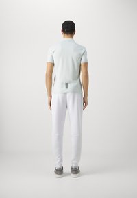 Light mint short-sleeve polo shirt with a subtle texture, paired with white sweatpants and gray sneakers, viewed from the back.