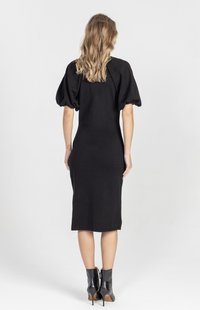 Czarna, sięgaj�ąca kolan sukienka z bufkami na rękawach, dopasowanym krojem i miękką fakturą. Noszona z czarnymi botkami na szpilce sięgającymi kostki.
