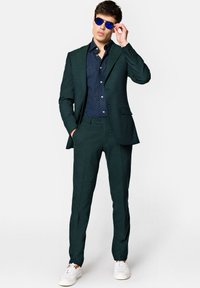Zielony garnitur o dopasowanym kroju, zestawiony z granatową koszulą w kropki. Uzupełniony niebieskimi okularami przeciwsłonecznymi i białymi trampkami.