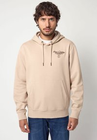 Sudadera de algodón beige con bolsillo frontal tipo canguro, capucha con cordones y sutil logo bordado en el pecho. Corte casual y puños acanalados.