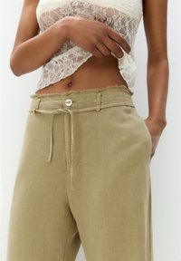 Lichtbeige linnen broek met een trekkoord in de taille, een rafelige zoom en een enkele knoopsluiting. Zachte textuur en een losse pasvorm.