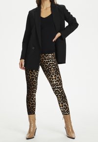 Černý blazer přes černý top, spojený s legínami s zvířecím potiskem, které mají zlaté a hnědé leopardí skvrny, a béžovými botami na podpatku.