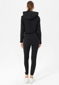 Felpa nera corta con cappuccio, abbinata a leggins neri slim-fit con pannelli laterali bianchi e polsini alle caviglie, completata da sneakers bianche.