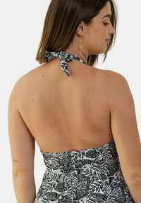 Robe halter en noir et blanc avec un motif de feuilles tropicales, tissu texturé et dos ouvert, dotée d'un détail noué au niveau du cou.
