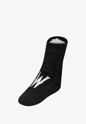 Czarna dziana skarpeta z wzorem w warkocz, wyściółka z runa i biały logo "W" z boku; długość do połowy łydki z zaokrąglonym czubkiem.