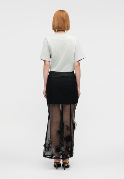 Γκρι τοπ με κοντά μανίκια σε συνδυασμό με μια διάφανη μαύρη φούστα με floral διακοσμήσεις και ενιαία μέση. Το σύνολο ολοκληρώνεται με παπούτσια με τακούνι.