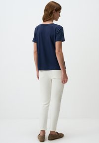 Marineblaues T-Shirt mit kurzen Ärmeln und lockerer Passform, kombiniert mit weißen Slim-Fit-Hosen und braunen Schuhen, von hinten betrachtet.